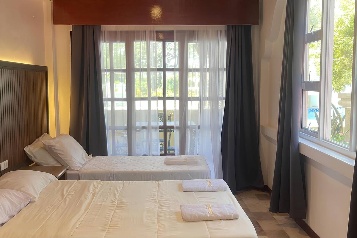 A hotel room with two beds, a wooden headboard, a large window with curtains, and a view of the outdoors.
