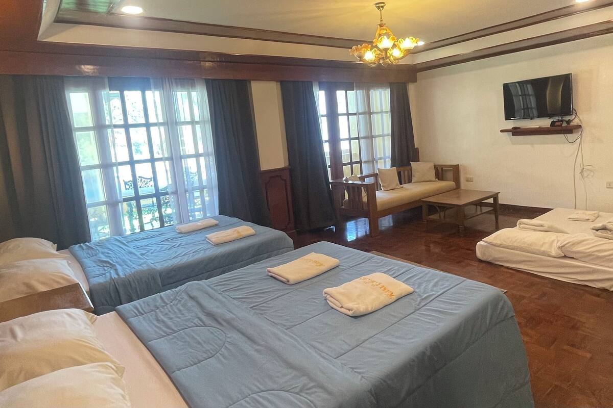 A hotel room with two beds, a sofa, a TV, and a chandelier.