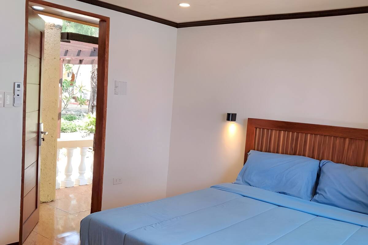 A bedroom with a bed, wooden headboard, ceiling fan, and a view of the outside through an open door.