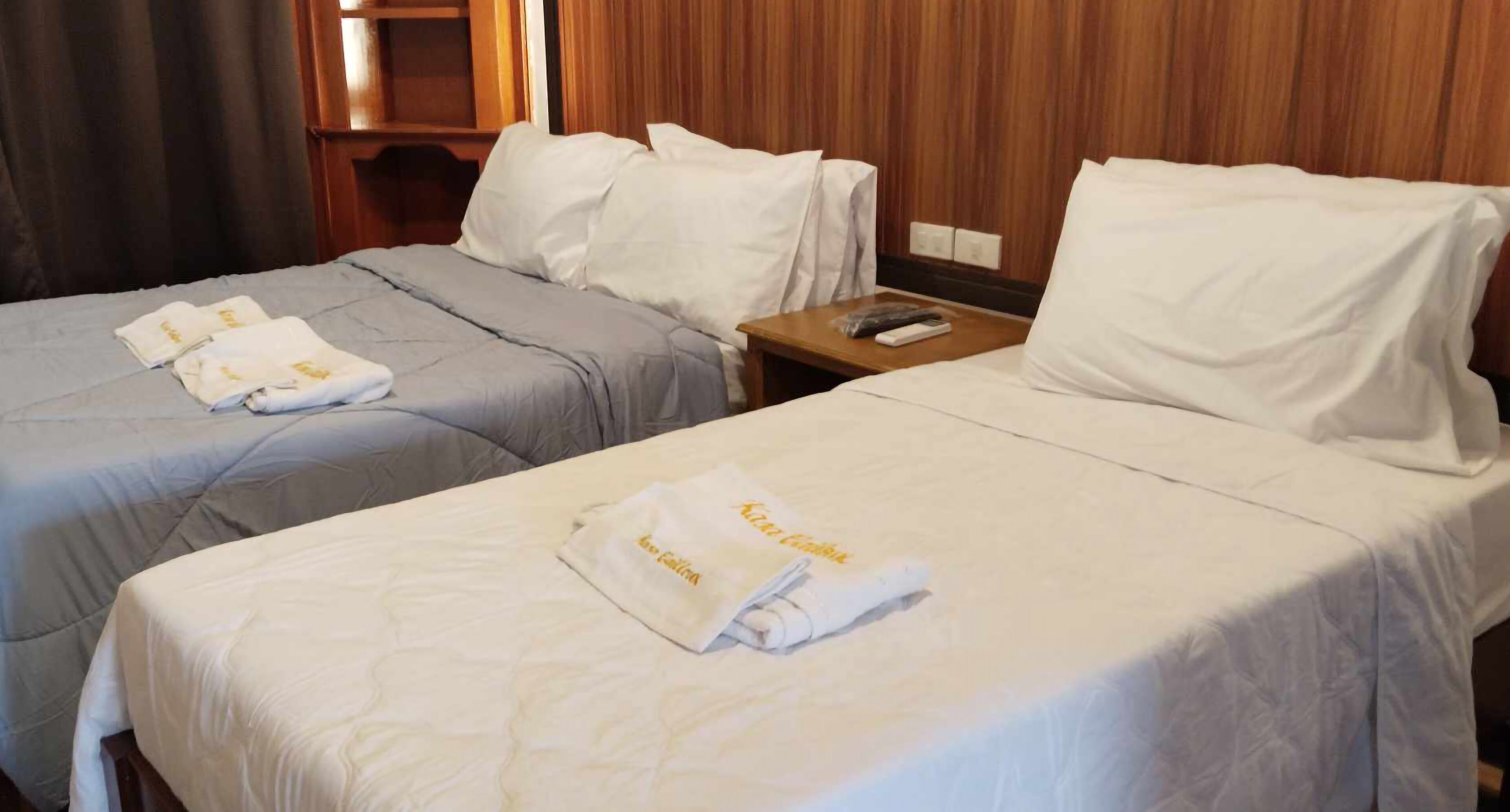 Two beds with white linens and towels, a wooden headboard, and a nightstand with a remote control.