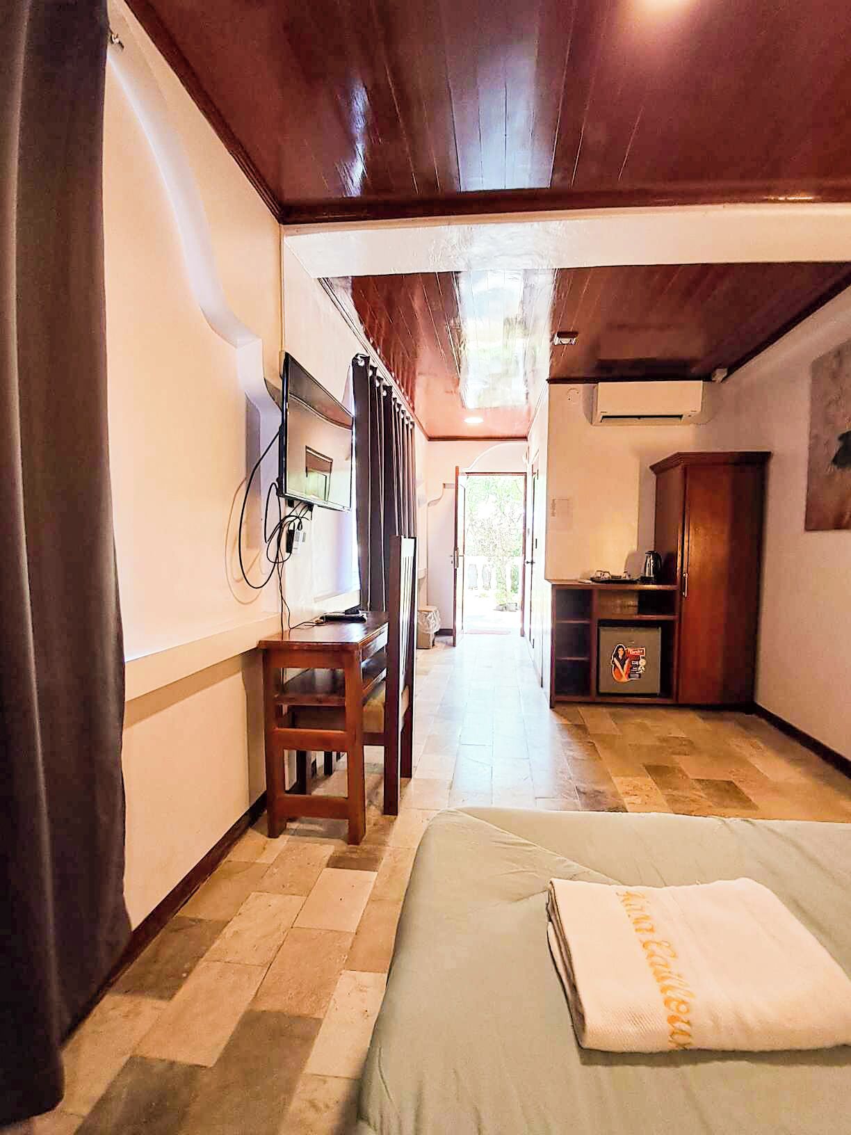 Habitación de hotel con cama, escritorio, silla, televisor y armario.