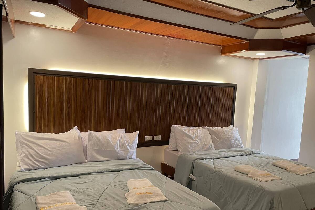 A hotel room with two beds, each with a wooden headboard and light-colored bedding.