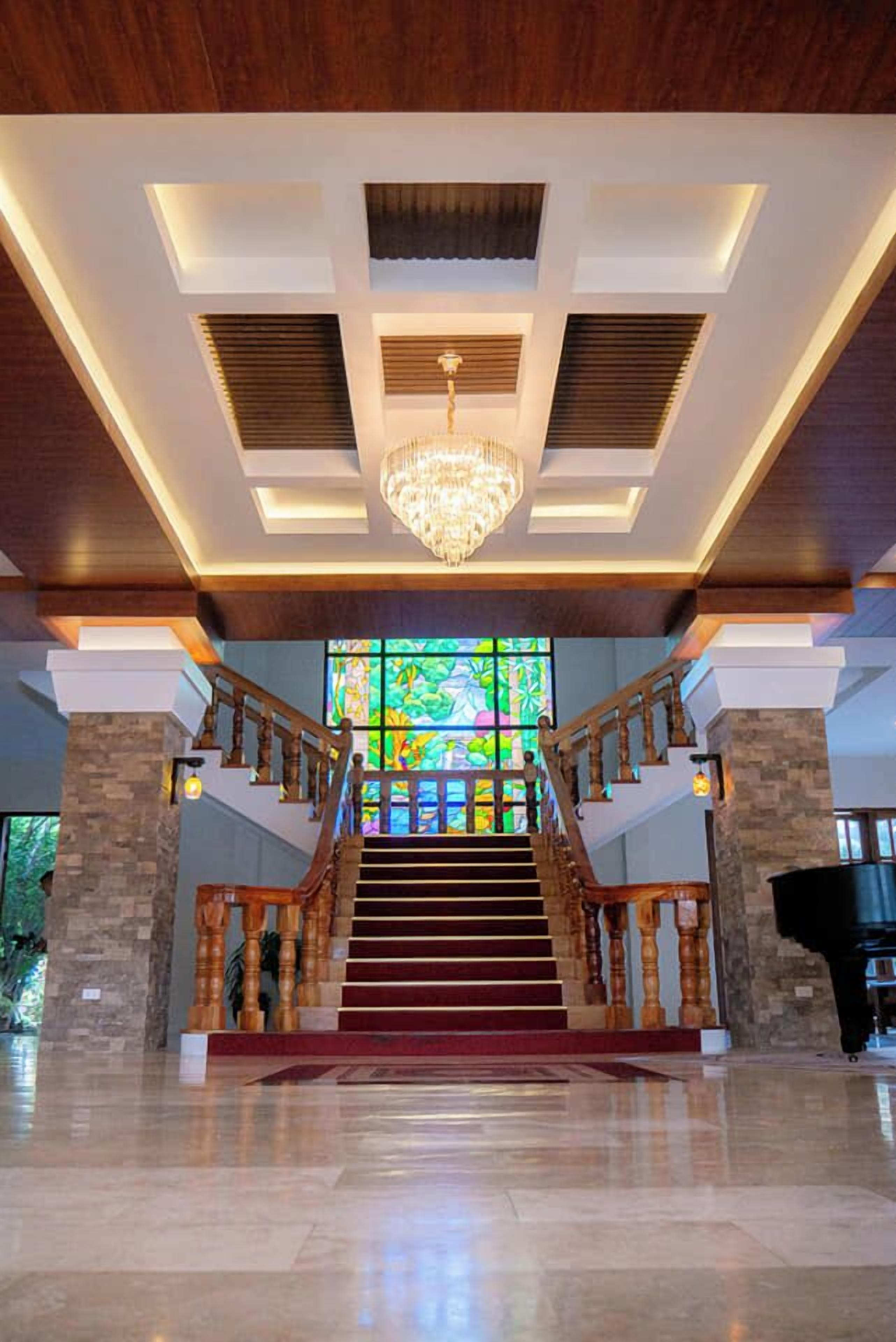 A grand staircase with wooden railings and a chandelier, leading to a stained glass window.