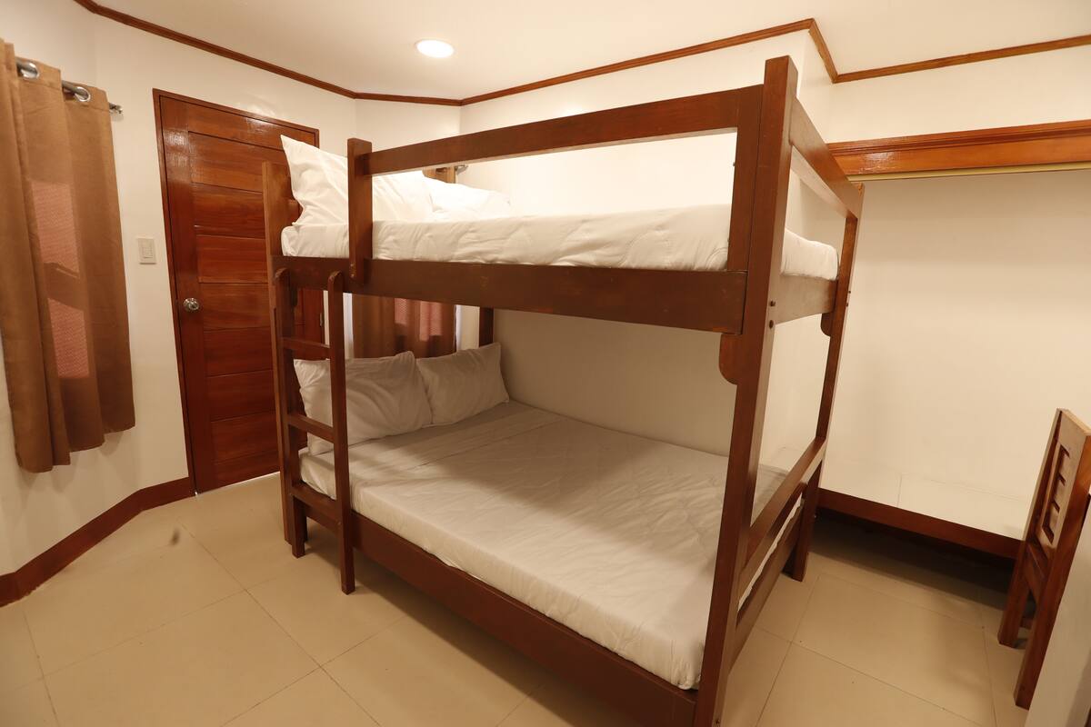 A bunk bed room with a wooden frame, a door, and a small wooden chair.