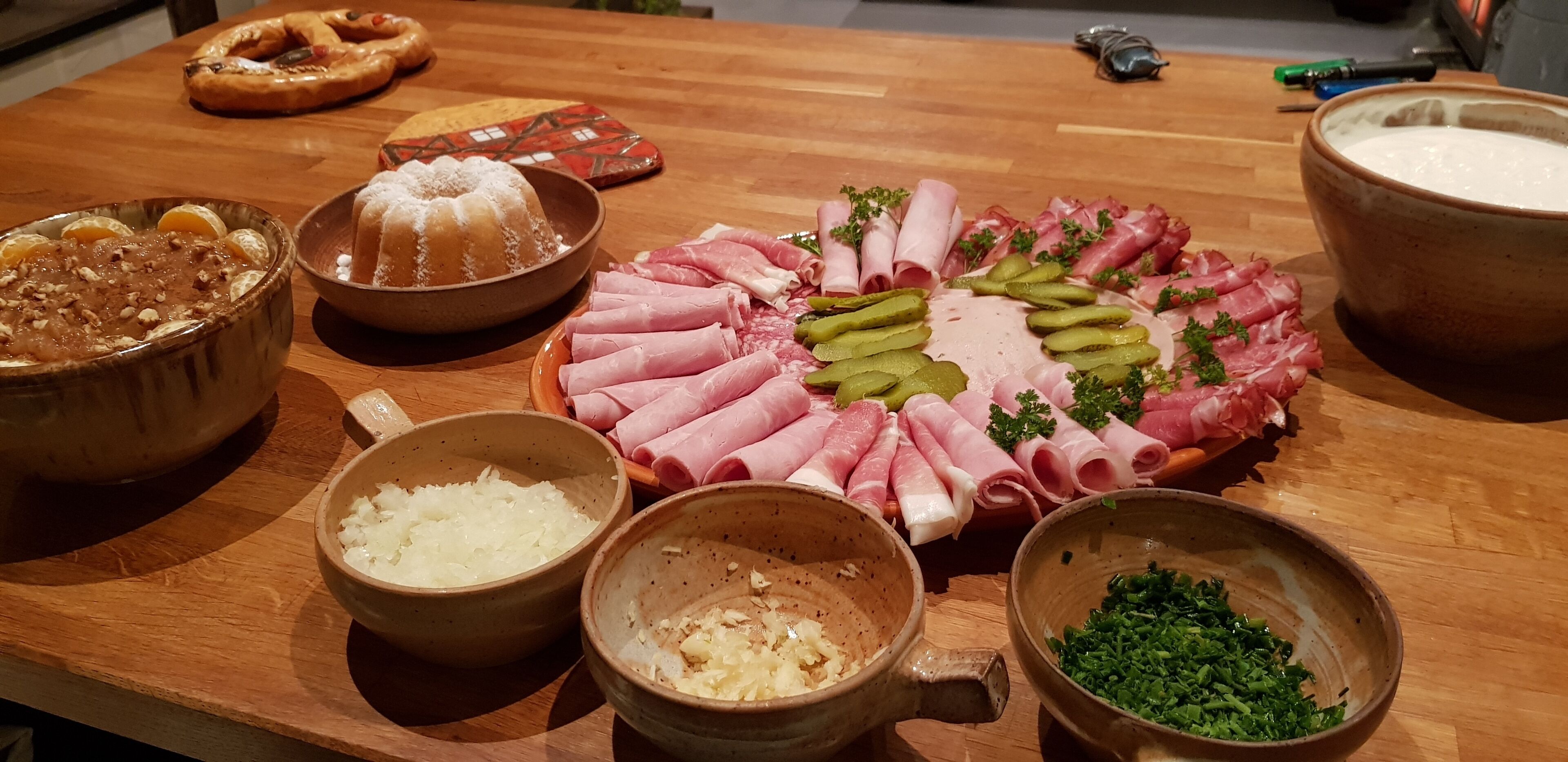 Une table en bois sur laquelle on trouve divers aliments, notamment un plateau de viandes, des bols contenant différents ingrédients et un bretzel.