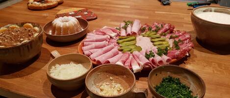 Une table en bois sur laquelle on trouve divers aliments, notamment un plateau de viandes, des bols contenant différents ingrédients et un bretzel.