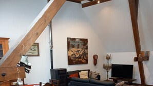 Uma sala de estar acolhedora com escada de madeira, mesa de jantar com cadeiras, sofá azul e televisão.