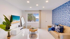 A modern living room with a white sofa, a coffee table, and a large window with a view of palm trees. - Modern Beachside: Restaurants, Pool (Hollywood)