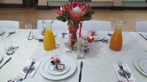 A dining table set with plates, cutlery, glasses, and a centerpiece with a red flower arrangement.