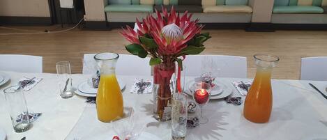 A dining table set with plates, cutlery, glasses, and a centerpiece with a red flower arrangement.