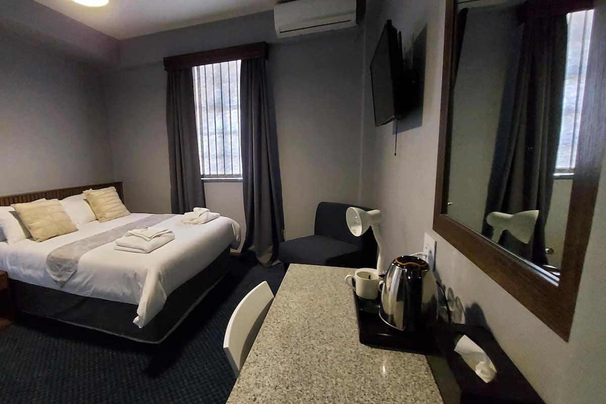 Une chambre d’hôtel équipée d’un lit, d’un bureau, d’une chaise, d’un miroir, d’une machine à café et d’une fenêtre avec des rideaux.