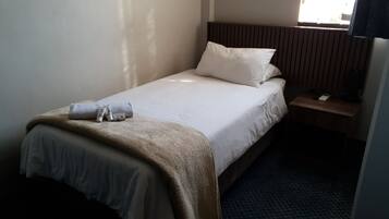 A hotel room with a single bed, a bedside table with a lamp, and a window with curtains.