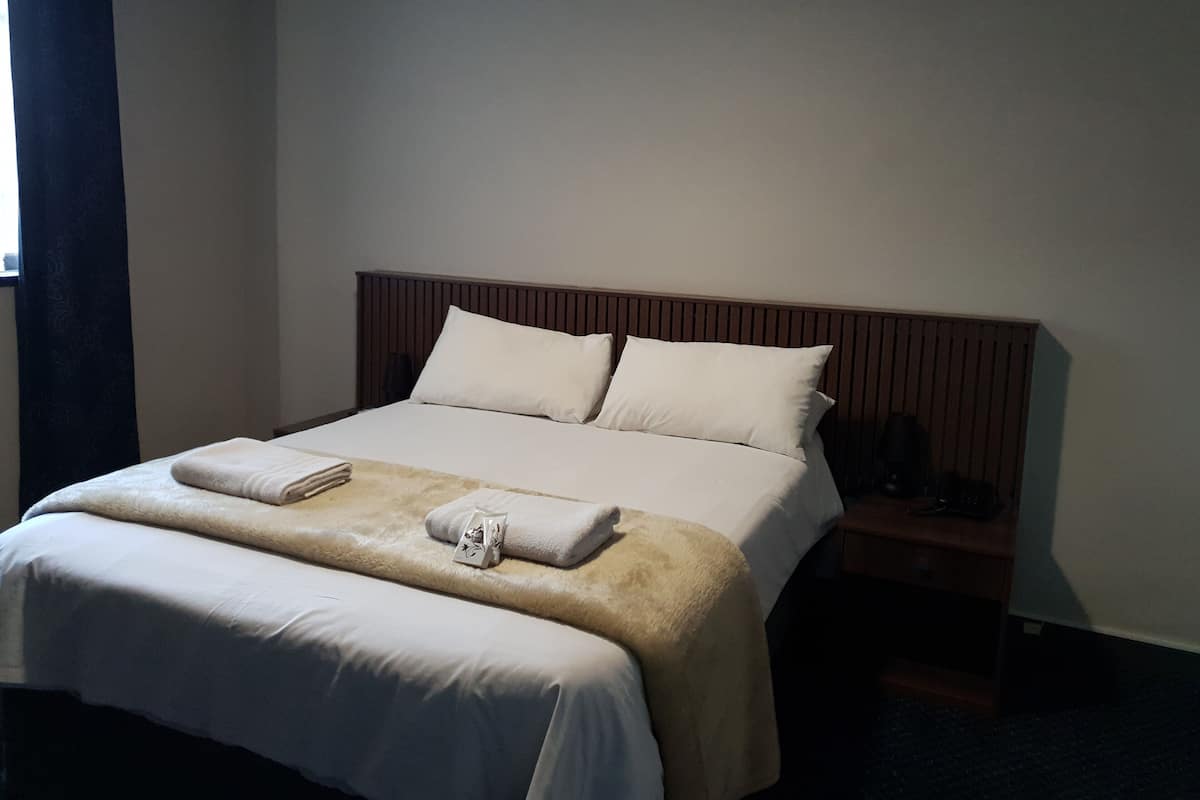 Un lit bien fait, avec du linge de lit blanc et deux oreillers, une tête de lit en bois et une table de chevet avec une lampe.