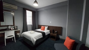 A hotel room with a bed, a desk, a chair, a nightstand, and a window.