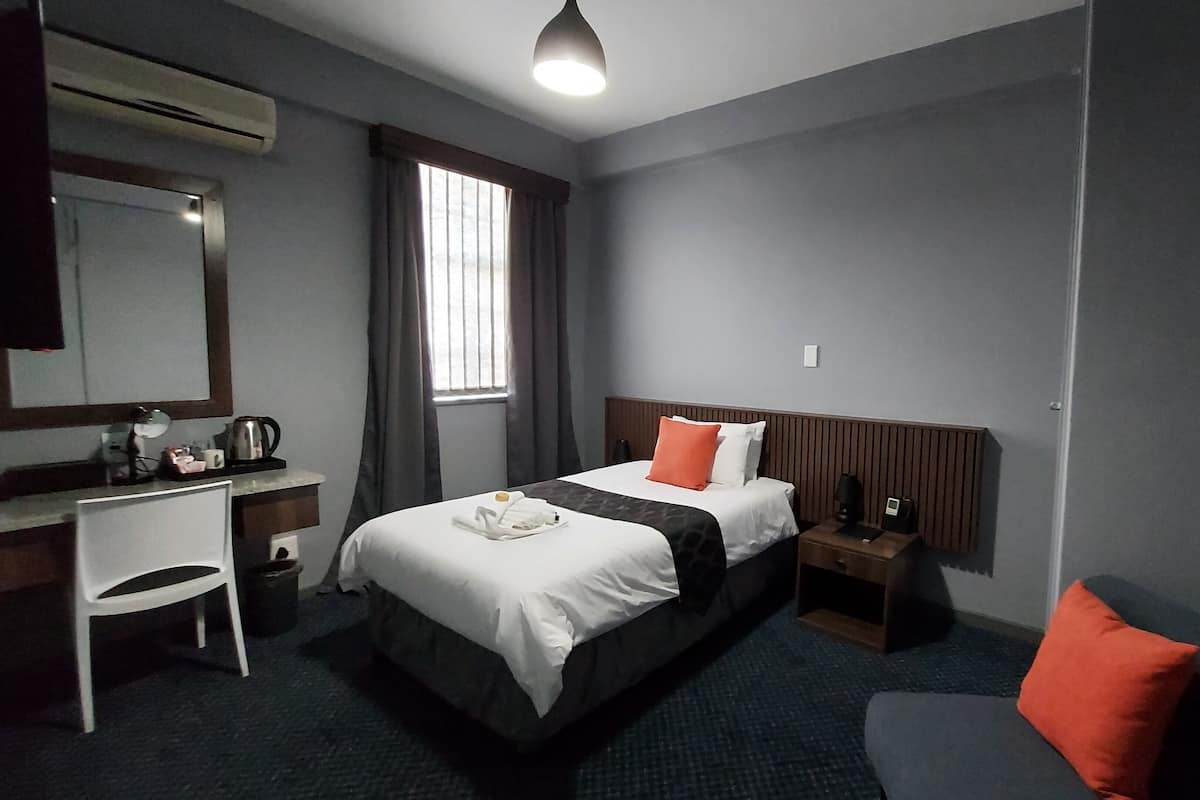 Une chambre d’hôtel avec un lit, un bureau, une chaise, une table de chevet et une fenêtre.