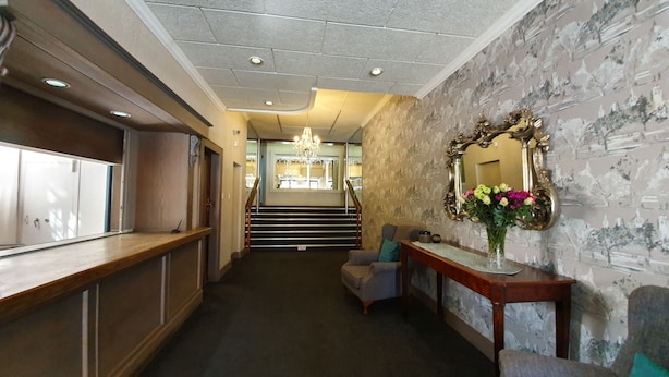 A hotel lobby with a reception desk, a staircase, and a seating area with a mirror and flowers.