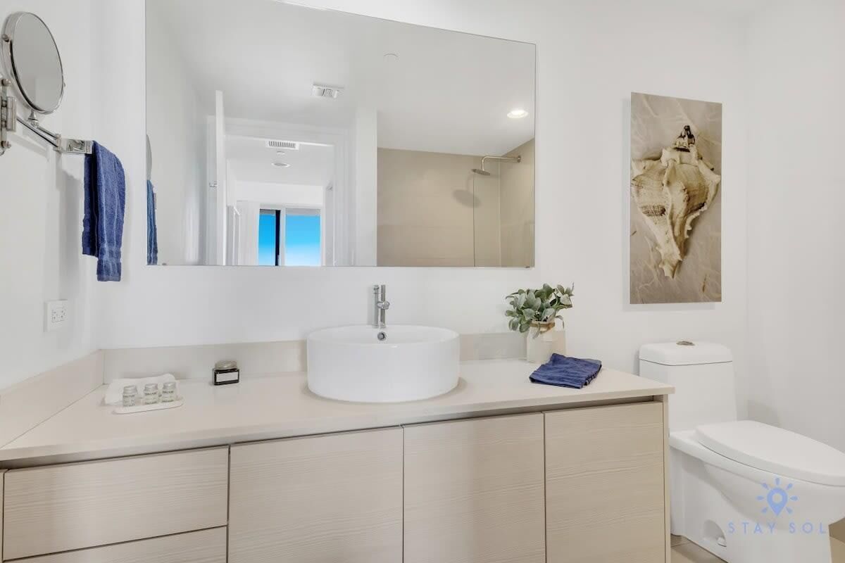 Un bany modern amb un lavabo rodó, un mirall gran, un vàter i una obra d'art penjada a la paret.
