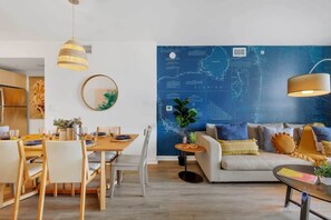 A modern living room with a large wall map, a dining area with wooden furniture, and a sofa with multiple cushions. - Resort Condo: Balcony, Pool, Ideal for Families (Hallandale Beach)