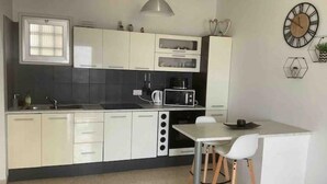 A modern kitchen with white cabinets, a black countertop, a microwave, and a dining area with a white table and two chairs. - Sunset view every night from your own balcony!

 (Paphos)