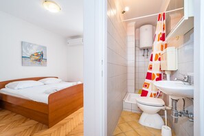 A bedroom with a wooden bed, a bathroom with a toilet, sink, and shower curtain.