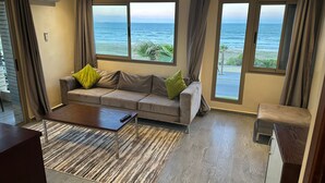 A living room with a sofa, a coffee table, and a view of the ocean through large windows. - Oceana Mazagan Suites Hotel  (El Jadida)