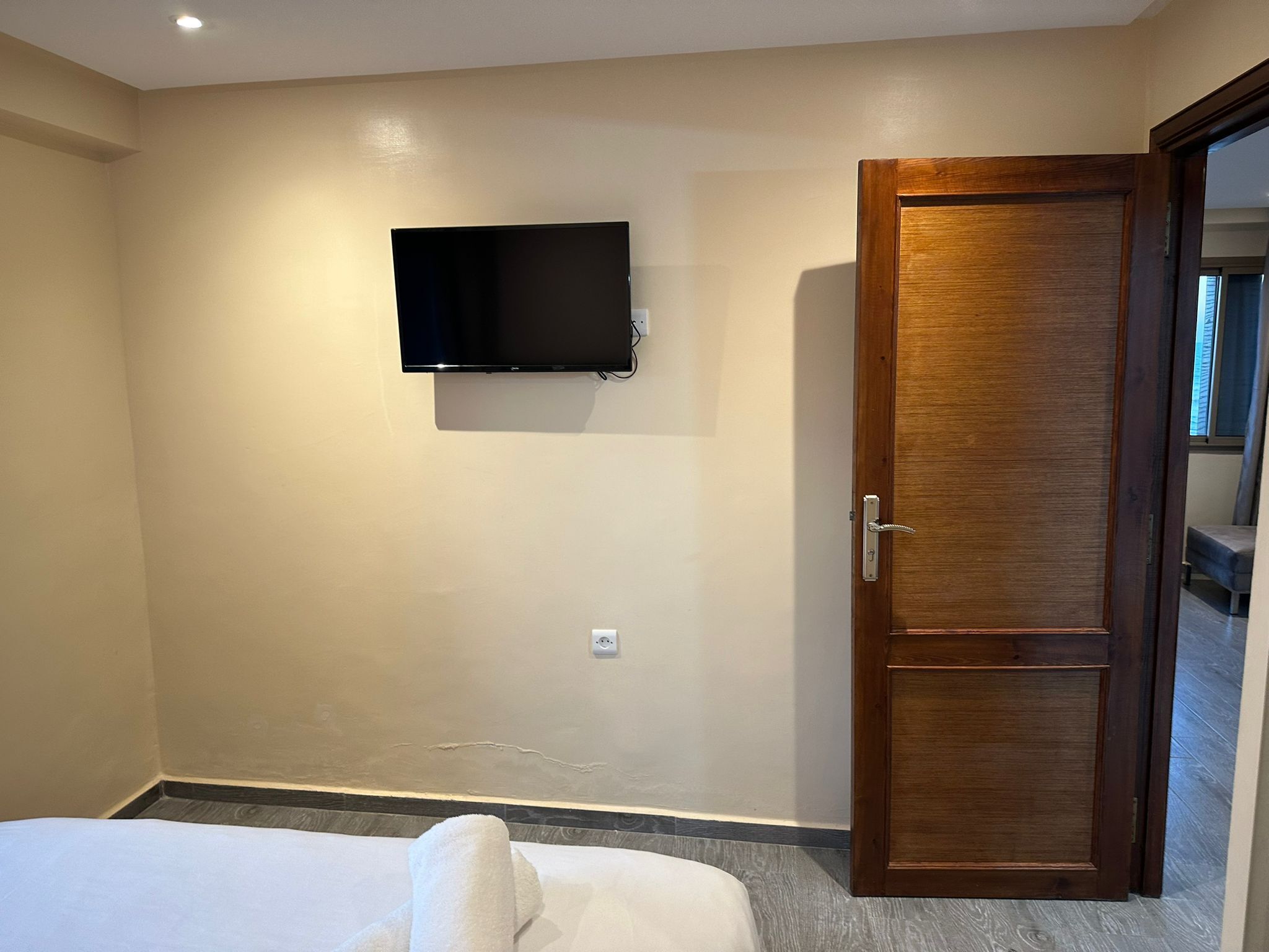 Una habitación de hotel con una cama, un televisor fijado en la pared y una puerta de madera.