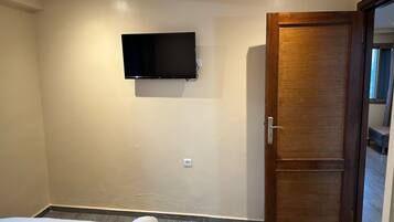 Una habitación de hotel con una cama, un televisor fijado en la pared y una puerta de madera.