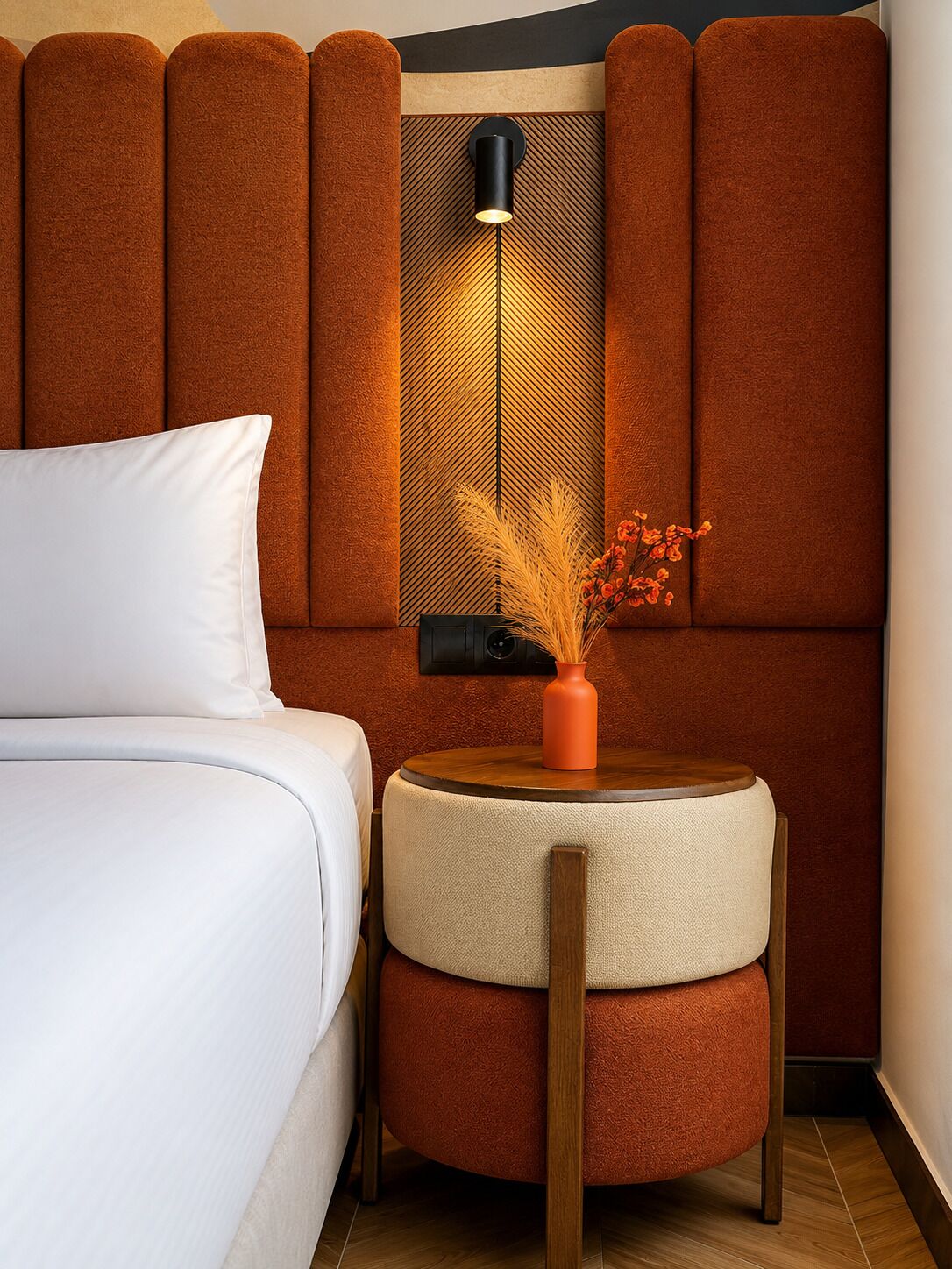 A hotel room with a bed, a small round table with a vase, and a wall-mounted lamp.