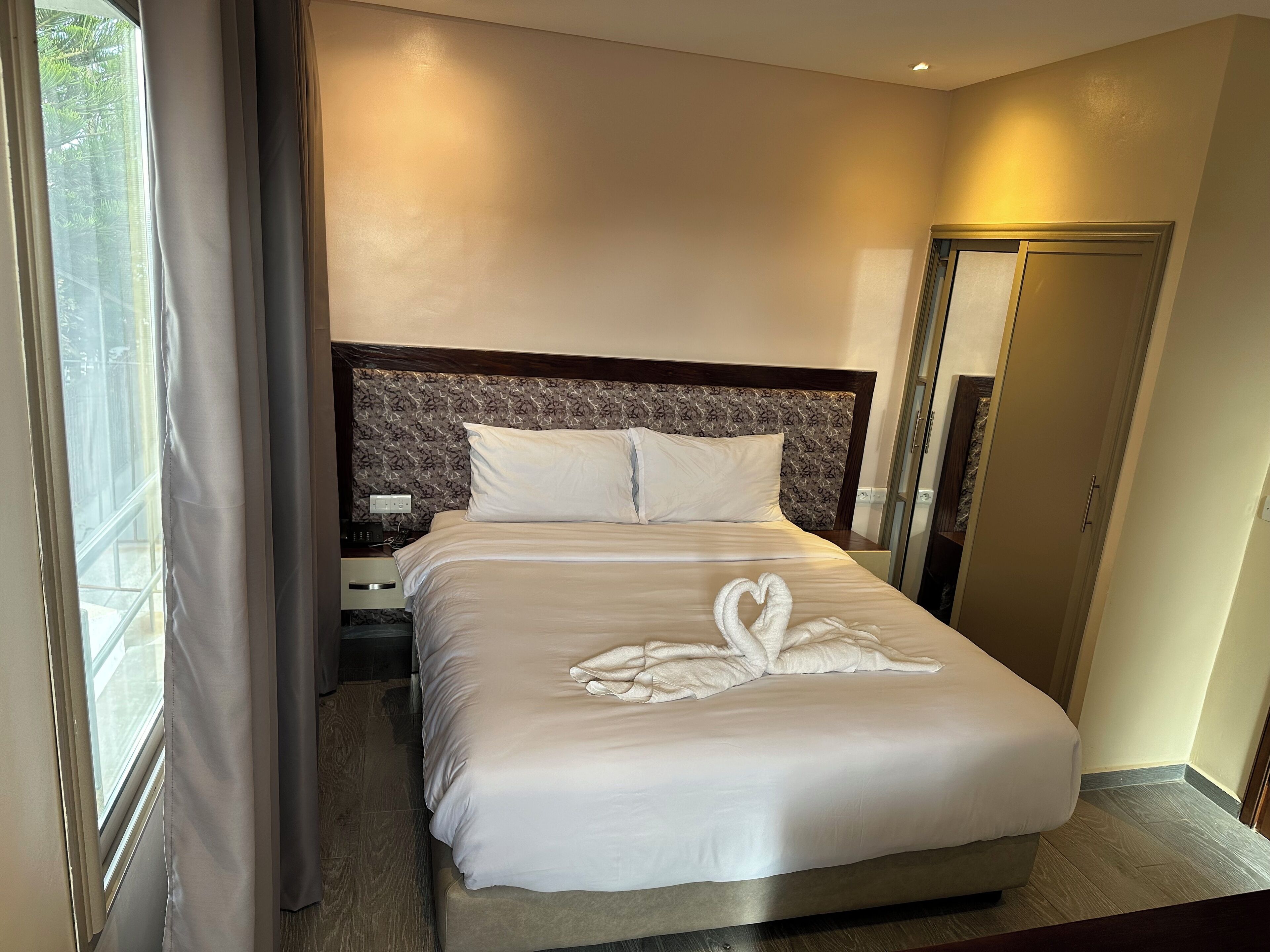Habitación de hotel con una cama bien hecha, una mesita de noche con teléfono y un espejo en la pared.