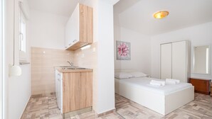 A modern bedroom with a large bed, a small kitchenette, and a bathroom with a mirror. - Studio Apartments Near Center 3 (Novalja)