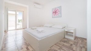 A bedroom with a bed, a nightstand, a painting, and a view through a glass door. - Studio Apartments Near Center 3 (Novalja)