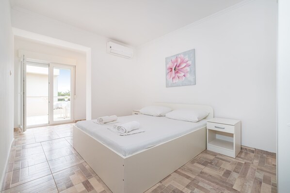 A bedroom with a bed, a nightstand, a painting, and a view through a glass door.