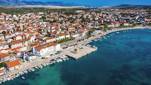 An aerial view of a coastal town with a marina, buildings with red roofs, and mountains in the background. - Studio Apartments Near Center 4 (Novalja)