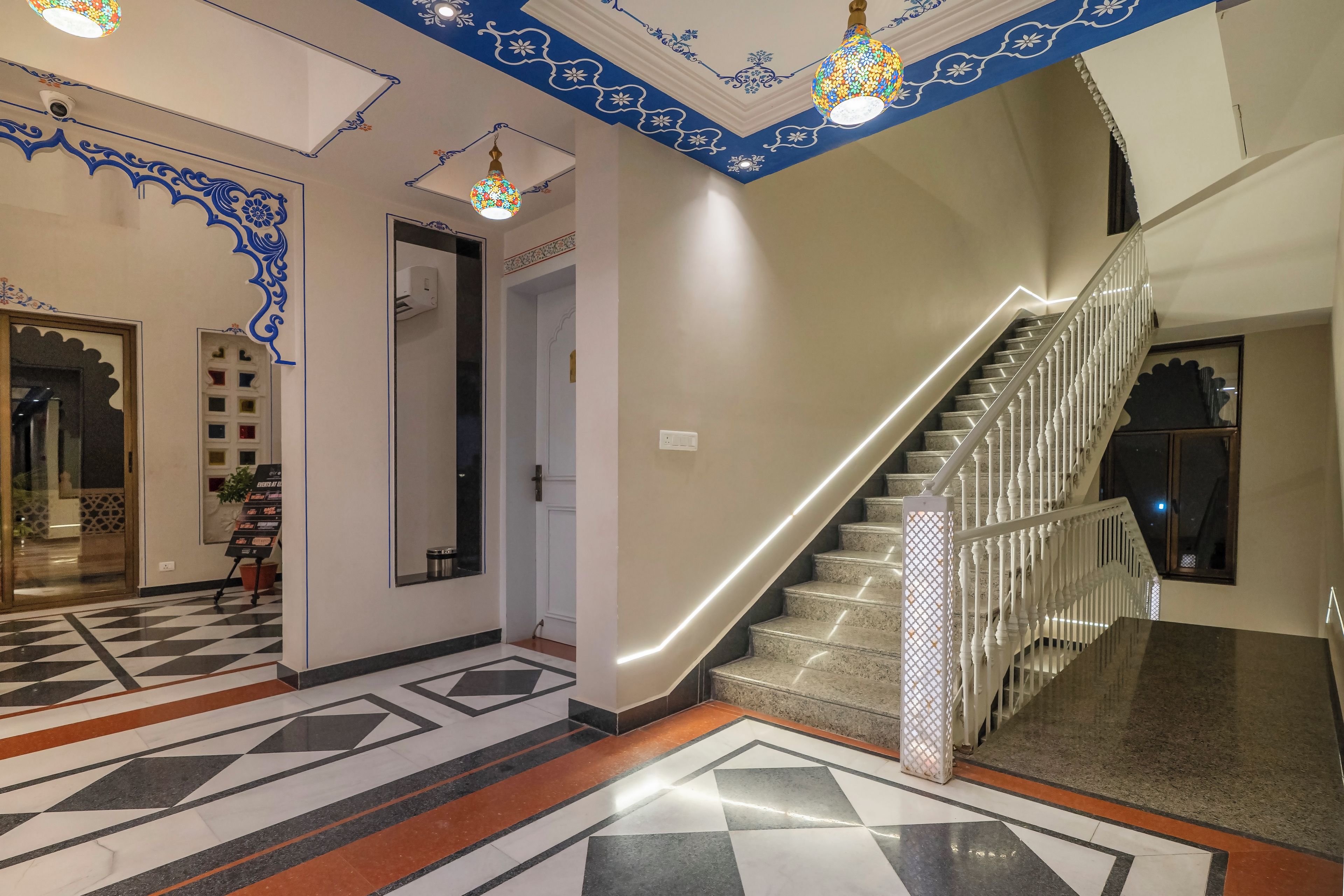 A hotel lobby with a geometric patterned floor, a staircase with white balusters, and decorative ceiling elements.