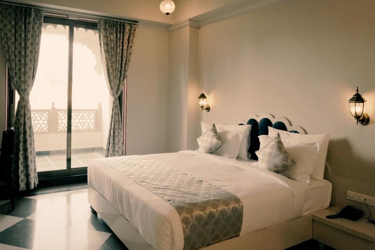 A hotel room with a bed, a desk, a chair, a nightstand, and a wall-mounted lamp.