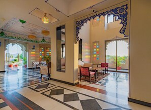 A hotel lobby with a checkered floor, seating area, decorative ceiling, and large windows. - The Biletha Bagh (Udaipur)