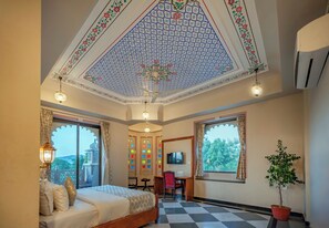 Une chambre d’hôtel avec un sol à carreaux, un lit avec des oreillers, un bureau avec une chaise, une télévision et une plante en pot.