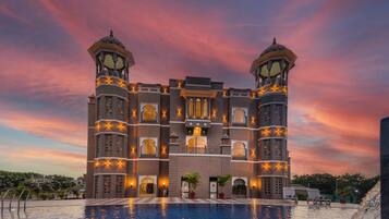 Un edificio grande con dos torres, una piscina y un cielo al atardecer.