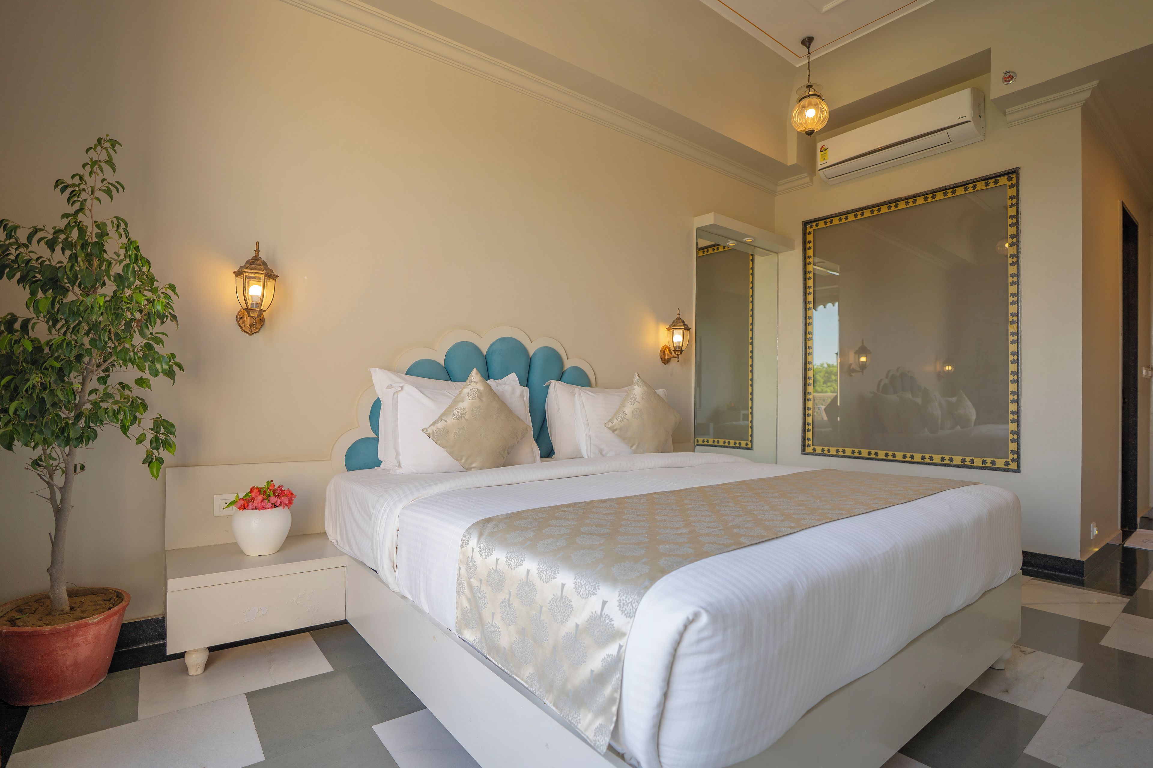 Una habitación de hotel con una cama grande, una planta en maceta, una mesita de noche y un espejo.
