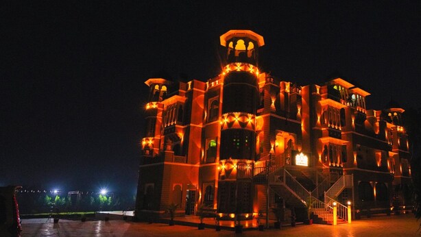 A large, illuminated building with multiple levels and balconies, featuring a grand entrance and a staircase leading to the upper floors. - The Biletha Bagh (Udaipur)
