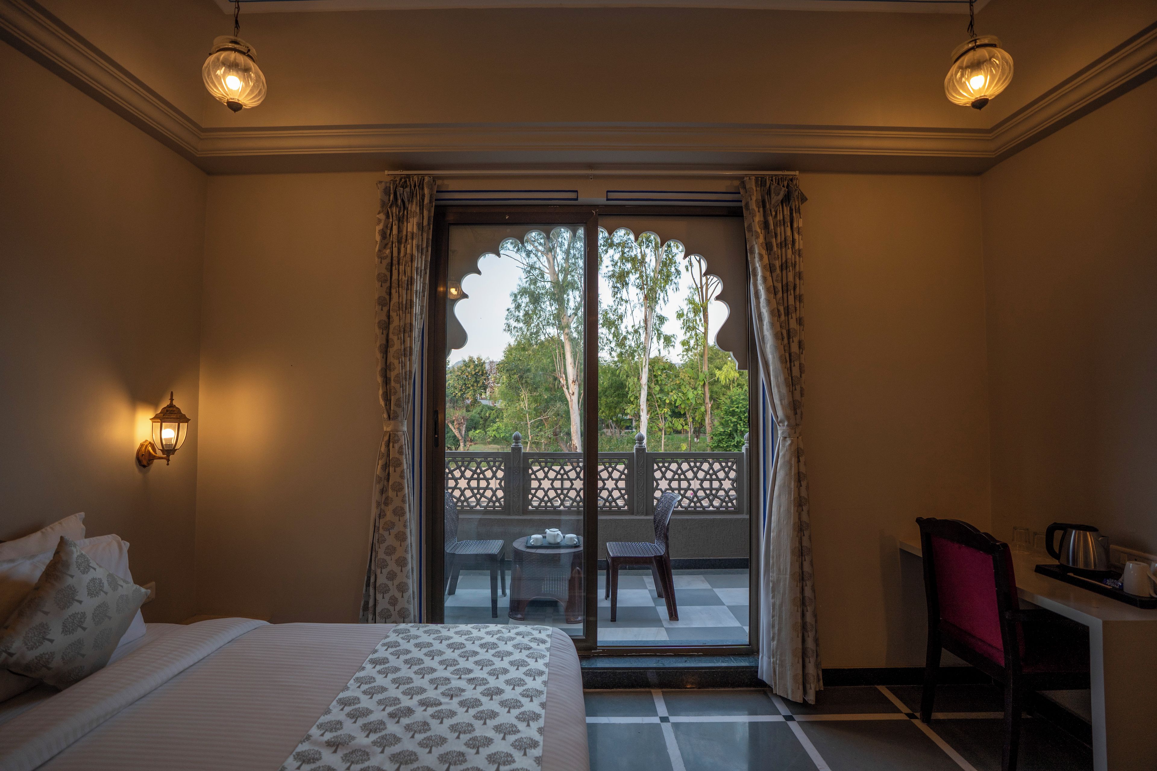 Habitación de hotel con cama, escritorio y balcón con vistas a árboles.