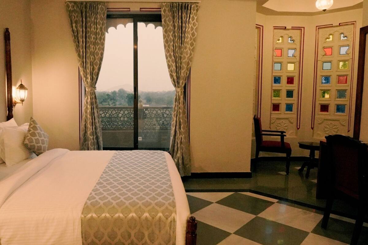 A hotel room with a bed, a desk, a chair, a television, and a balcony with patterned doors.