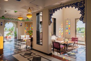 A hotel lobby with a checkered floor, seating area with patterned chairs, decorative wall art, and a large mirror. - The Biletha Bagh (Udaipur)