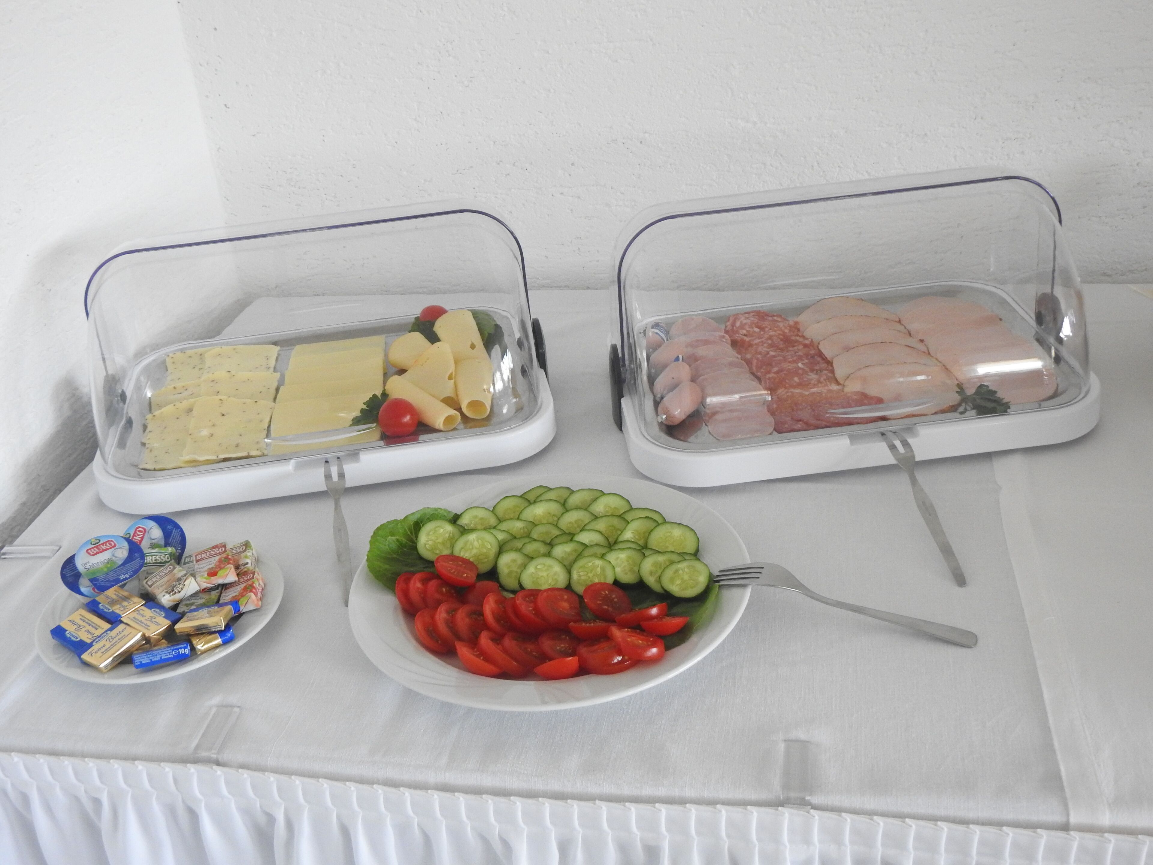 Une table de buffet proposant divers plats, notamment des pâtes, de la viande et une assiette de légumes coupés.
