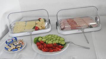 Une table de buffet proposant divers plats, notamment des pâtes, de la viande et une assiette de légumes coupés.