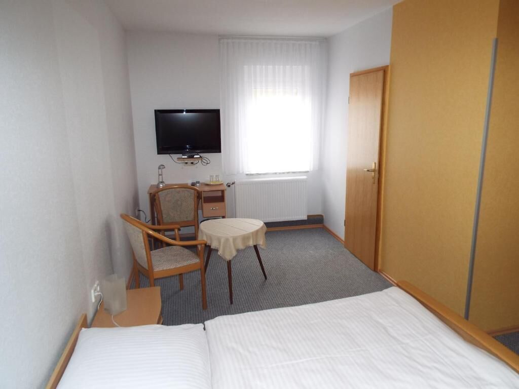 Une chambre d’hôtel avec un lit, une télévision, une chaise, une petite table et une fenêtre avec des rideaux.