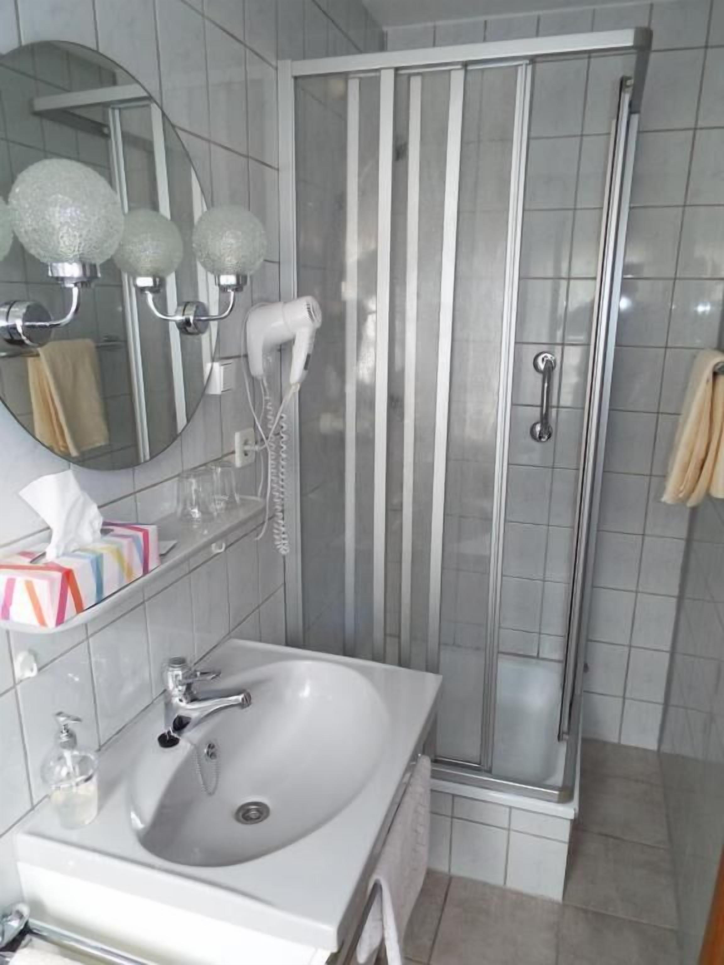 Ein Badezimmer mit einem weißen Waschbecken, einem Spiegel und einer Duschkabine aus Glas.
