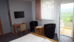 Habitación de hotel con cama, escritorio, silla, televisor y vista al exterior a través de una puerta corredera.