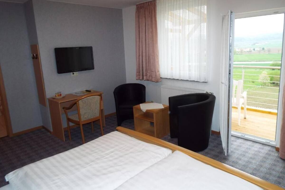 Habitación de hotel con cama, escritorio, silla, televisor y vista al exterior a través de una puerta corredera.
