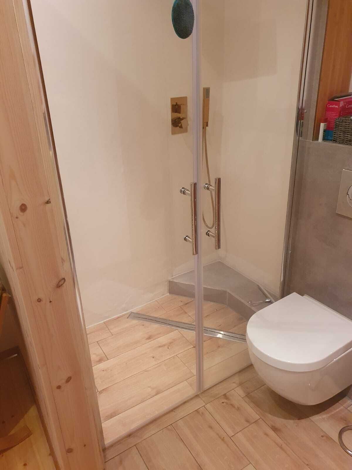 A small bathroom with a shower, toilet, and wooden flooring.